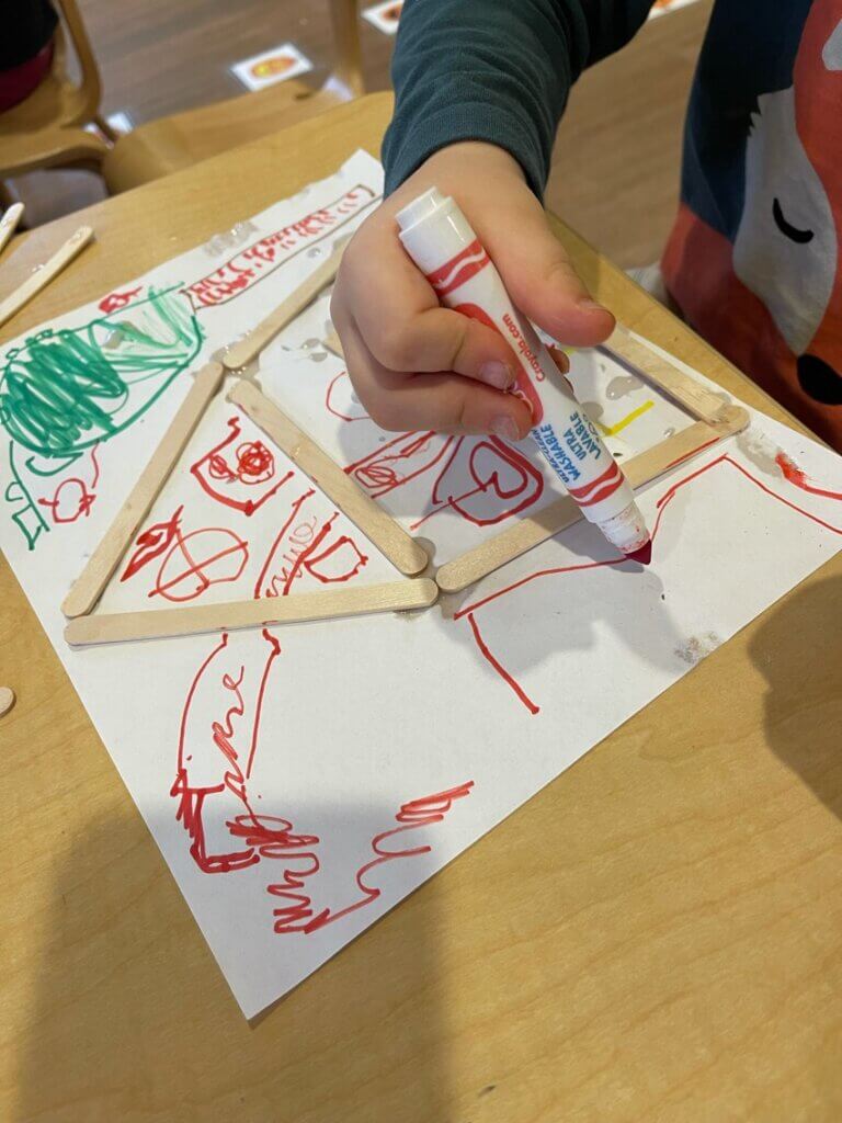 A child drawing a house with markers and popsicle sticks at Early Learning For Everyone